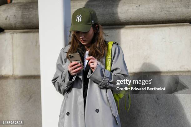 Guest wears a khaki denim with embroidered NY logo pattern cap from New Era, a gray long coat, a green shiny leather shoulder bag, dark gray wide...