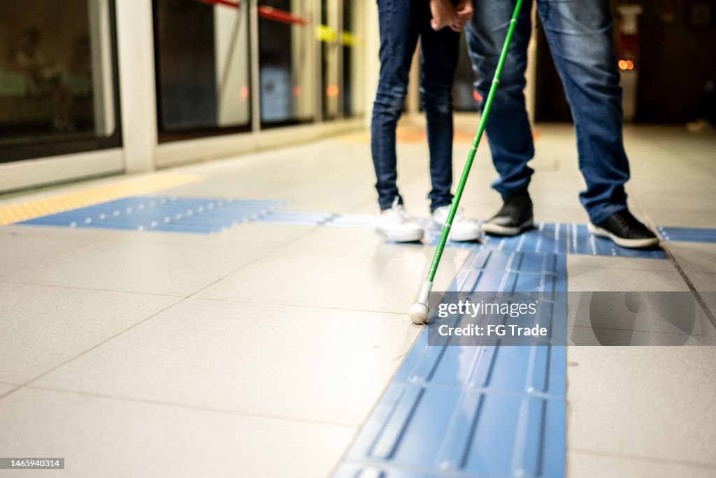 Seção baixa de um pai cego e uma filha em uma estação de metrô
