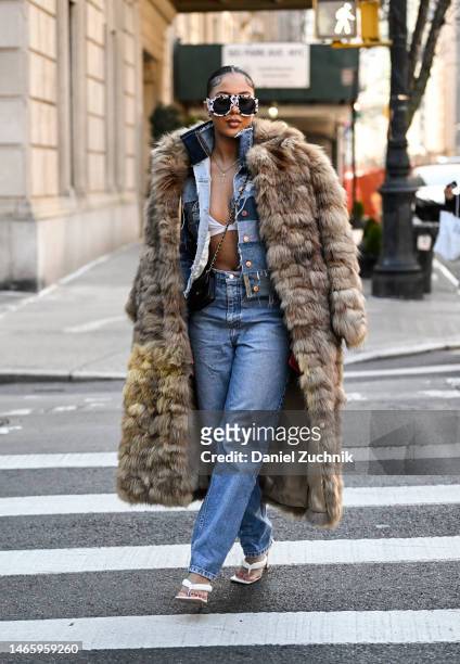 Guest is seen wearing a brown faux fur coat, jean top and blue jean pants with black and white sunglasses outside the Dennis Basso show during New...