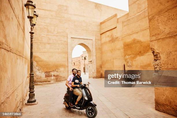 wide shot friends riding moped through the streets of marrakech - cobblestone transport stock pictures, royalty-free photos & images