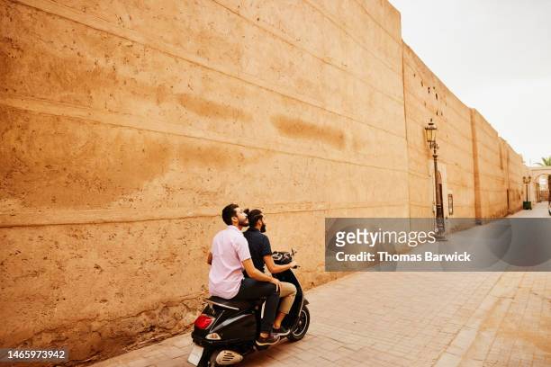 wide shot friends riding moped through the streets of marrakech - cobblestone stock pictures, royalty-free photos & images