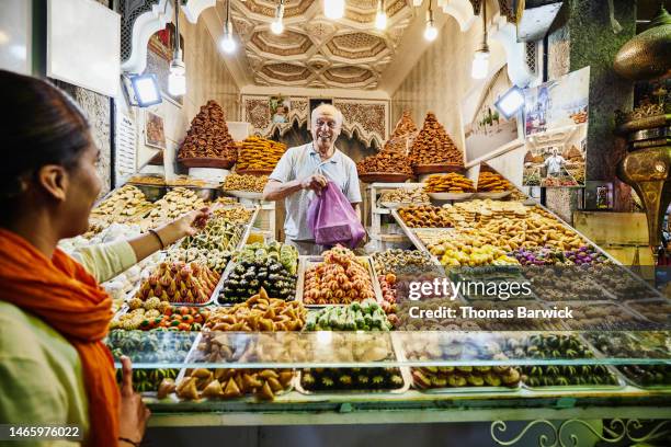 wide shot of smiling pastry shop owner taking payment from customer - zoco fotografías e imágenes de stock