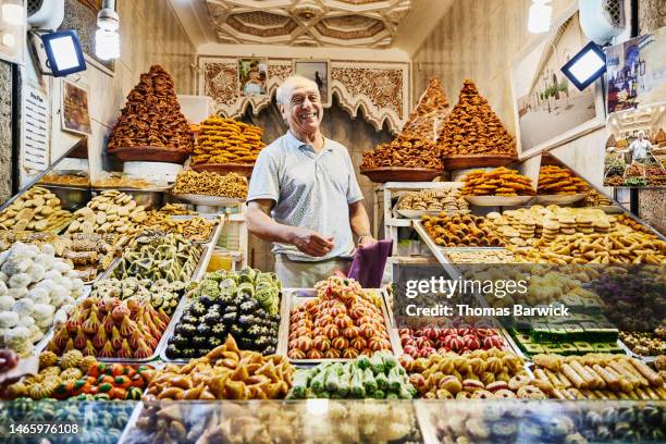 wide shot pastry shop owner standing in shop in the souks of marrakech - marktstand stock-fotos und bilder