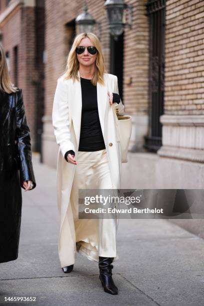 Guest wears black aviator sunglasses, a black long sleeves t-shirt, a white long wool coat, a white latte matte leather shoulder bag, a white silk...