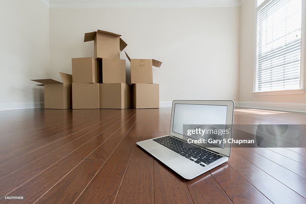 Blank laptop and moving boxes in an empty room