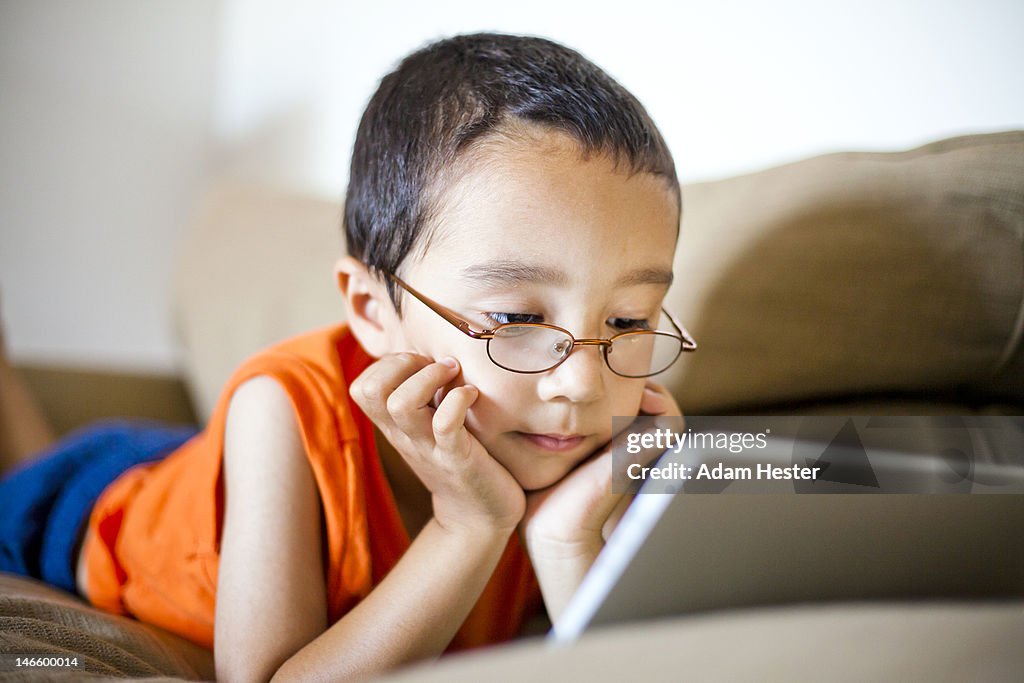 A young boy using a tablet device on a couch.