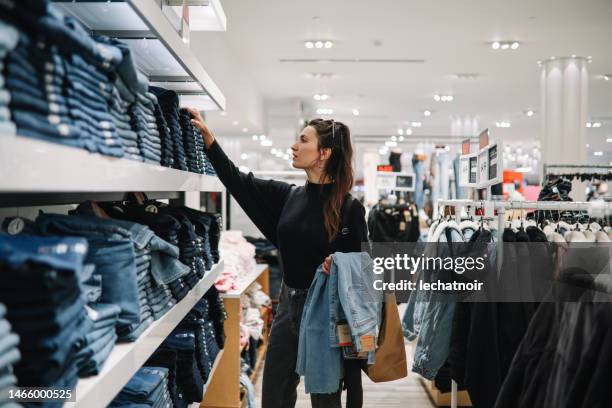 frau kauft jeans in einem bekleidungsgeschäft - jeans stock-fotos und bilder