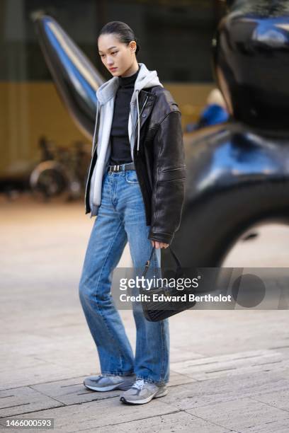 Guest wears a black turtleneck pullover, a pale gray zipper hoodie sweater, a black shiny leather oversized jacket, a black shiny leather belt, blue...