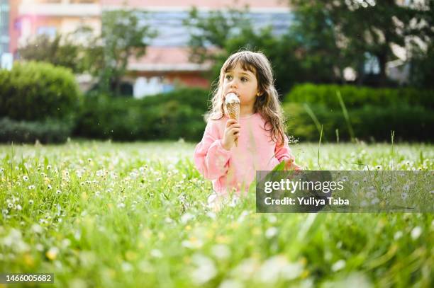 süßes kleines mädchen, das die frühlingsnatur genießt und eis in einem frühlingspark isst. - a cone stock-fotos und bilder