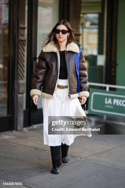 Guest wears black sunglasses, silver earrings, a black t-shirt, a dark brown shiny leather with beige sheep interior zipper aviator coat, a royal...