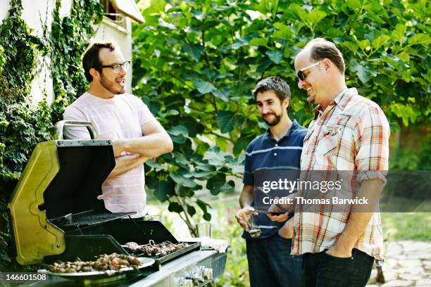 group of friends standing around while barbecuing - barbecue man stock pictures, royalty-free photos & images