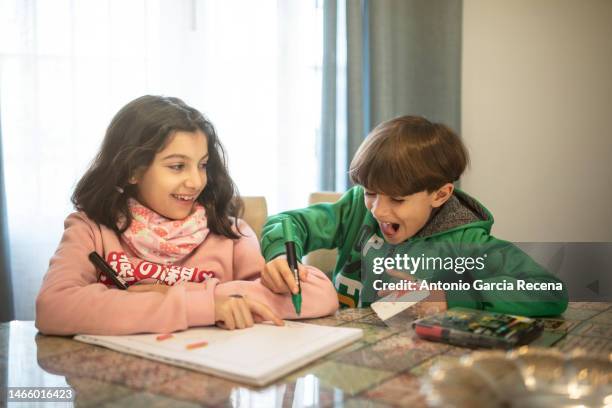 little siblings color and do homework together at home, smiling and playing while doing homework - waskrijttekening stockfoto's en -beelden