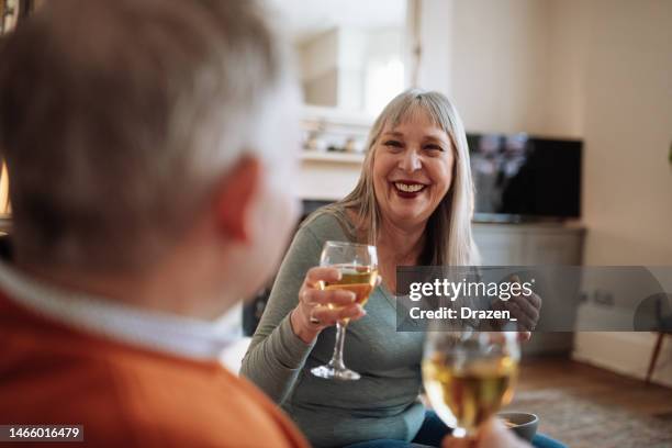 romance among seniors - two grey hair vital seniors sitting on couch and drinking white wine - day in the life series stock pictures, royalty-free photos & images