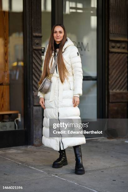 Guest wears a black high neck / cut-out neck pullover, a white hoodie quilted long puffer jacket from Mackage, a gray shiny leather crossbody bag,...