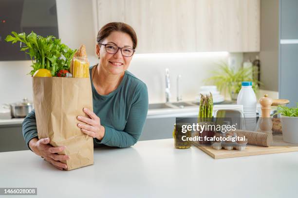 confident woman holding groceries shopping bag on kitchen counter - bag fresh stock pictures, royalty-free photos & images