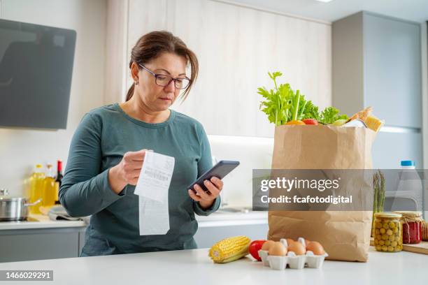 mujer que usa un teléfono inteligente revisando el recibo después de comprar comestibles - medios impresos fotografías e imágenes de stock