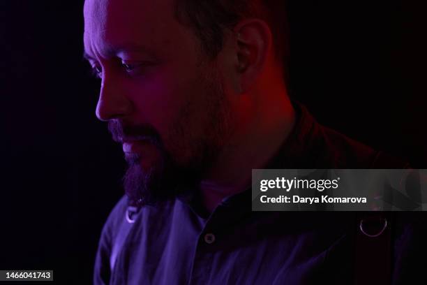 a  man with beard in the in a uniform with neon light purple and red looks away. the concept of the sadness, thoughtfulness, deep thoughts. black background with copy space. - red light portrait stock pictures, royalty-free photos & images