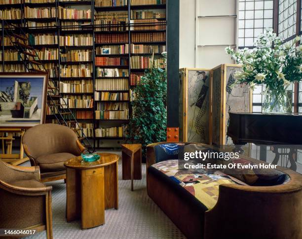 View of armchairs, a sofa, and bookcase in the living room at the Maison de Verre, Paris, France, 1982.