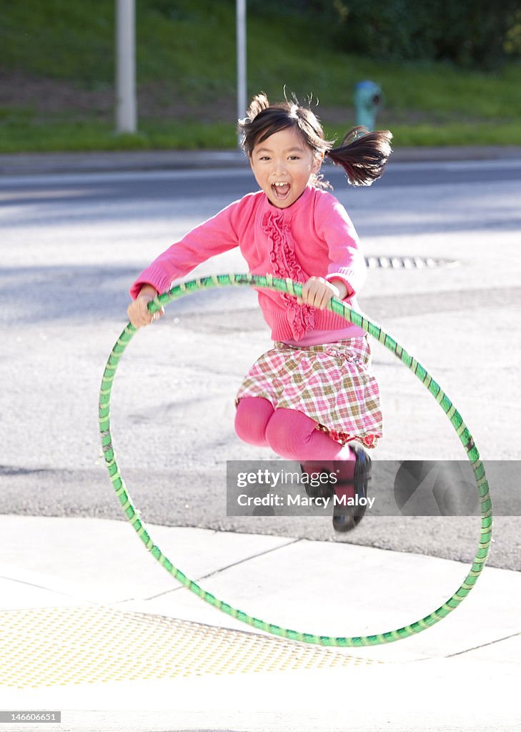 Smiling girl in pink jumping through a hula hoop.