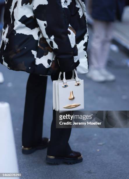 Guest wears a puffer jacket with cow spots pattern, black pants, brown and golden square toe boots and Schiaparelli bag outside before Proenza...