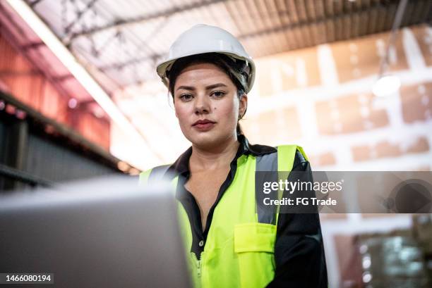 portrait of a young woman working on the laptop in a warehouse - construction worker pose stock pictures, royalty-free photos & images