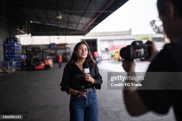 reporter talking on the microphone in a warehouse - jornalista imagens e fotografias de stock