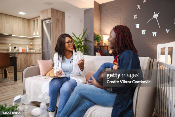 black female healthcare worker visiting mother and her son at home, while mother is breastfeeding - nurse with baby stock pictures, royalty-free photos & images