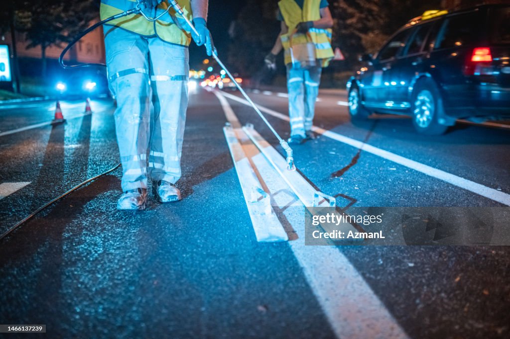 Road Maintenance Crew Repainting A Middle Lane Using A Spray Gun
