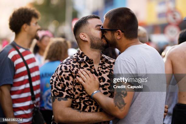 schwules paar küsst sich auf einer karnevalsparty - gay parade stock-fotos und bilder