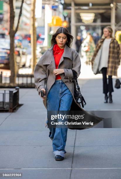 Guest wears grey coat, red top, denim jeans outside Brandon Maxwell during New York Fashion Week on February 14, 2023 in New York City.