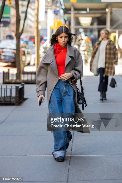 Guest wears grey coat, red top, denim jeans outside Brandon Maxwell during New York Fashion Week on February 14, 2023 in New York City.