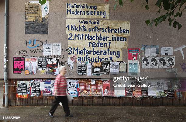 An elderly woman walks past a wall covered with left-wing posters and text that reads: "Rent Increase, Modernization . . . What to do? 1. Don't sign...