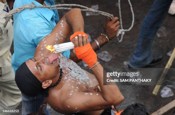 An Indian man drops hot melting wax onto his tongue and upper torso as he performs during the 135th Lord Jagannath Rath Yatra in Ahmedabad on June...