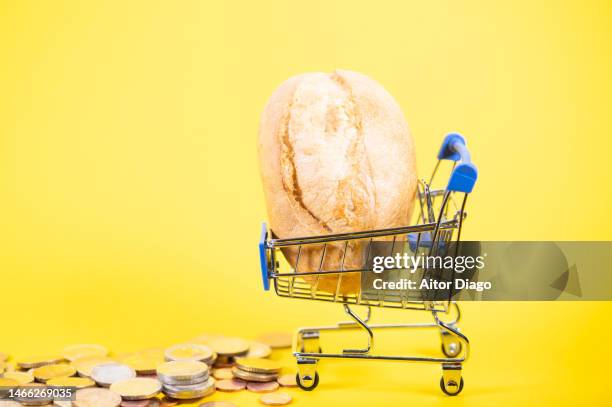 a shopping trolley with a loaf of bread and some coin on the floor. concept of rising prices of the shopping basket/ inflation - brot einkaufen stock-fotos und bilder