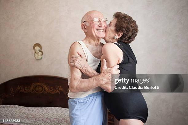 happy elderly couple hugging in a bedroom - happy couple cuddle stockfoto's en -beelden