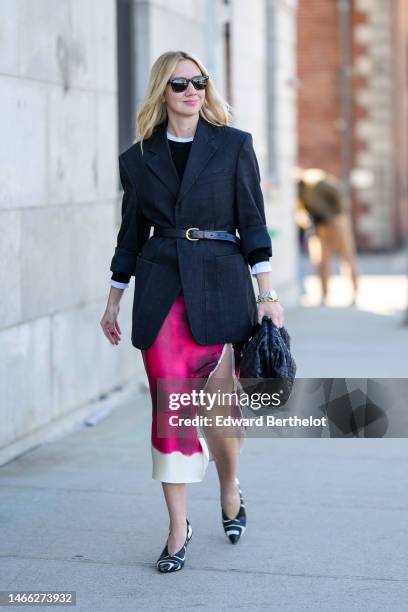 Lisa Aiken wears black sunglasses from Ray Ban, gold small earrings, a white t-shirt, a black sweater, a black linen blazer jacket, a black shiny...