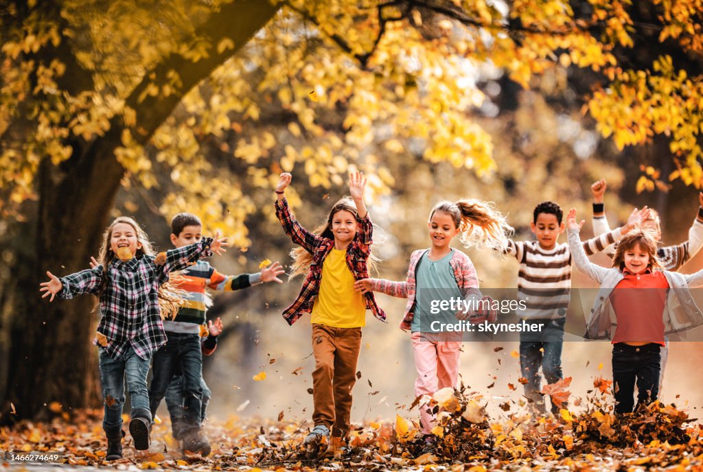 Large group of happy kids running through autumn leaves in the park.