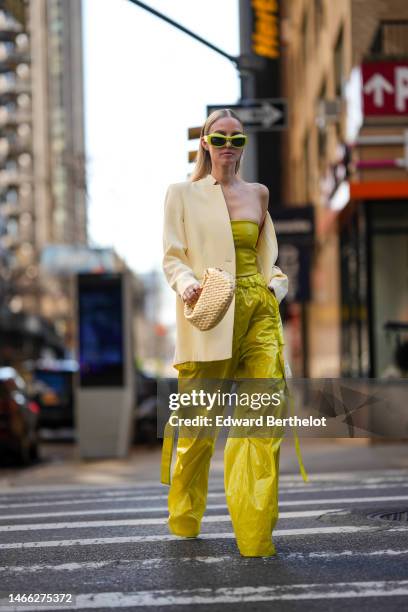 Leonie Hanne wears green puffy sunglasses, a beige oversized blazer jacket, a green shoulder off / cropped top, green silk satin large cargo pants, a...