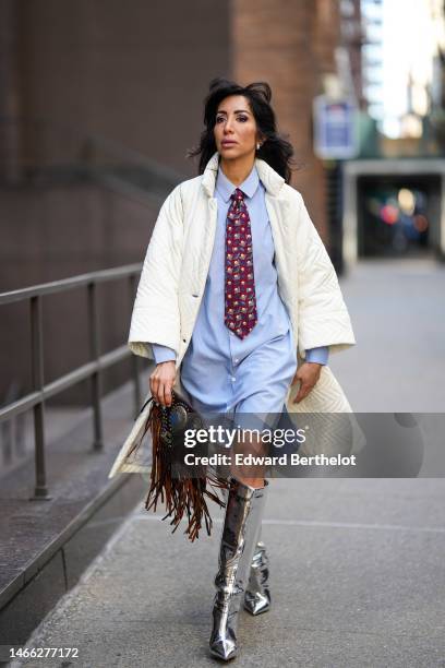 Ghizlane Sabbahe wears silver earrings, a pale blue shirt knees dress, a red/ purple / blue / gray / beige print pattern tie, a white latte quilted...