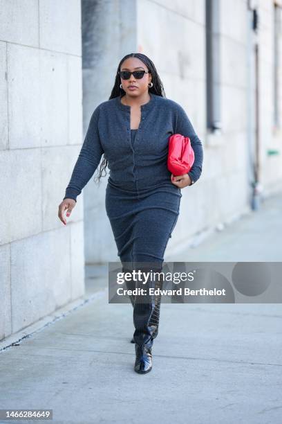 Guest wears black sunglasses, silver earrings, a dark gray buttoned wool cardigan, a matching dark gray knees dress, a red shiny leather puffy...