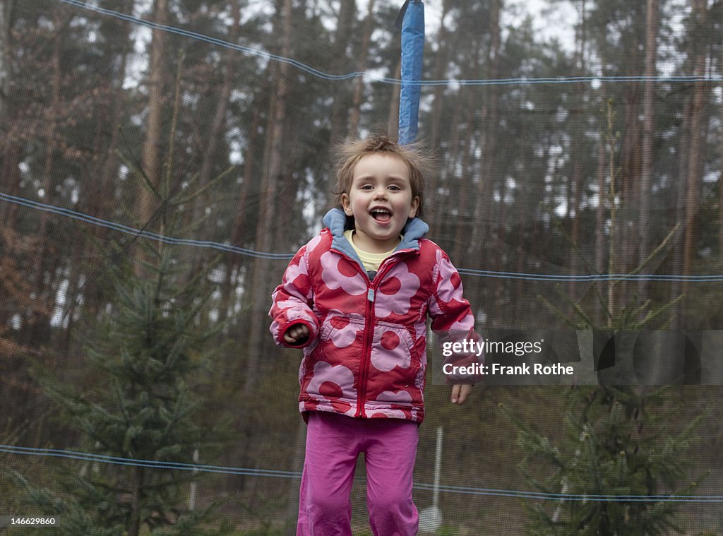 A young kid jumps on a trampoline in a forest