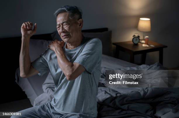 schlaflosigkeit älterer asiatischer mann, der nachts an nacken- und schulterschmerzen leidet. - arm um schulter stock-fotos und bilder