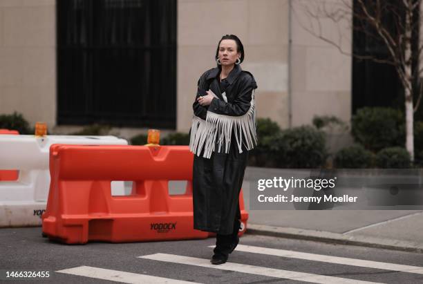 Guest wears silver rhinestones earrings, a black shiny leather long coat with embroidered white fringed sleeves, black suit pants, black shiny...