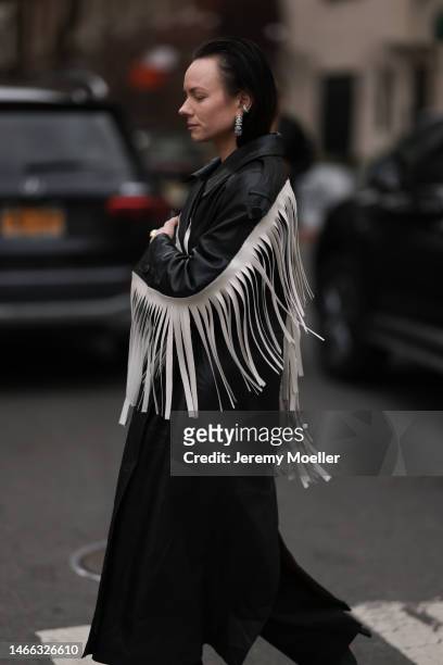 Guest wears silver rhinestones earrings, a black shiny leather long coat with embroidered white fringed sleeves, black suit pants, black shiny...