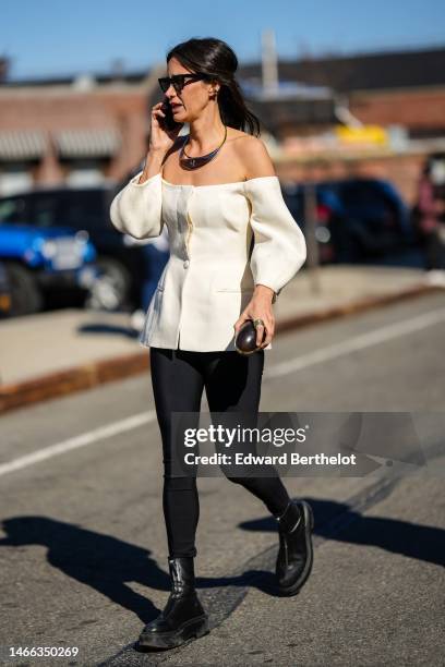 Guest wears black sunglasses, gold earrings, a gold and brown wool large necklace, a white latte shoulder-off / puffy sleeves / buttoned top, black...