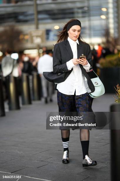 Guest wears a black large headband, silver earrings, a white shirt, a dark gray blazer jacket, a white shiny leather handbag, black and navy blue...