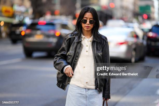 Guest wears black sunglasses from Ray Ban, a god necklace, a white t-shirt, a beige embossed mesh pattern sweater, a black shiny leather zipper...