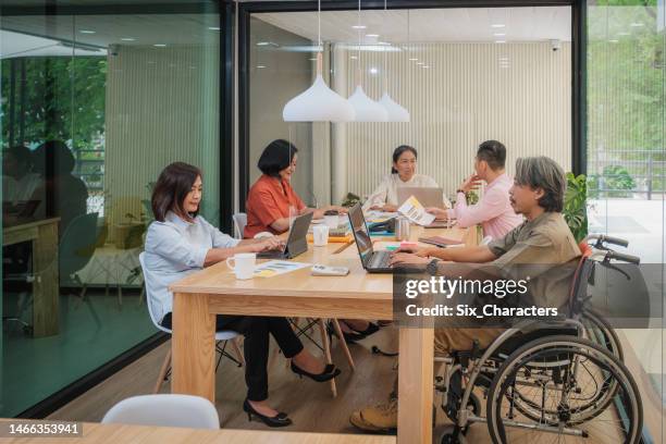 petit groupe d’asiatiques diversifient les personnes collègues avec un homme d’affaires handicapé en fauteuil roulant travaillant ensemble et discutant d’un nouveau projet dans un bureau moderne - small business meeting in asia photos et images de collection