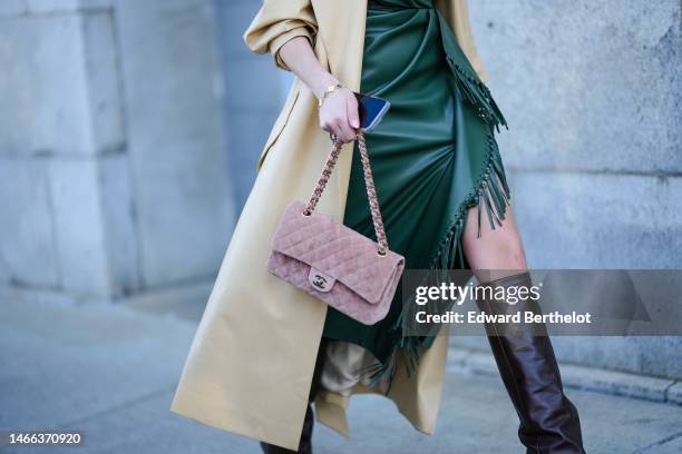 Guest wears a dark green shiny leather V-neck / wrap asymmetric knees dress with embroidered fringed borders, a pale yellow shiny leather long coat,...