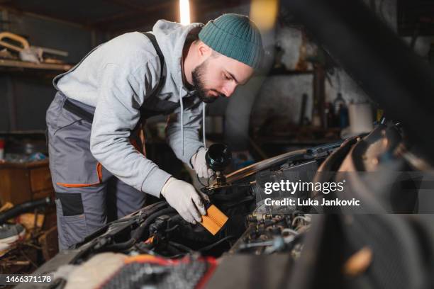 joven mecánico instalando un nuevo filtro de aceite en un coche en su garaje - filtración fotografías e imágenes de stock